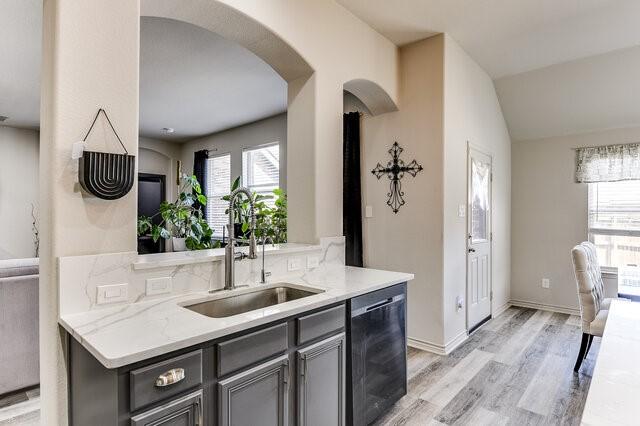 kitchen with light wood-type flooring, gray cabinetry, a sink, arched walkways, and dishwasher