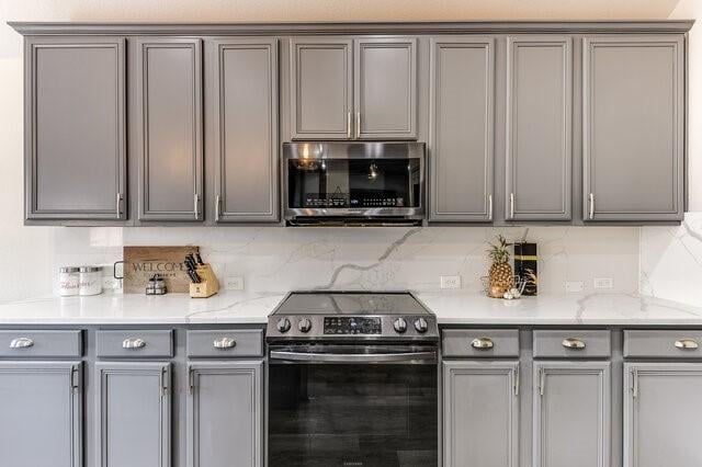 kitchen featuring decorative backsplash, stainless steel appliances, gray cabinets, and light stone counters