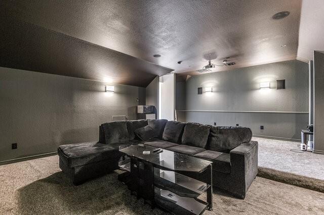 carpeted cinema with a textured wall, vaulted ceiling, and a textured ceiling