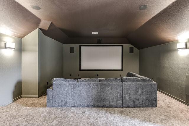 carpeted home theater room featuring baseboards, lofted ceiling, a textured wall, and a textured ceiling
