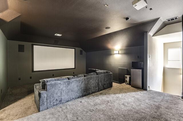 carpeted cinema room with vaulted ceiling, visible vents, and a textured ceiling