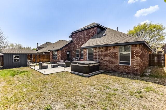 back of property with a patio, a fenced backyard, brick siding, a hot tub, and an outbuilding