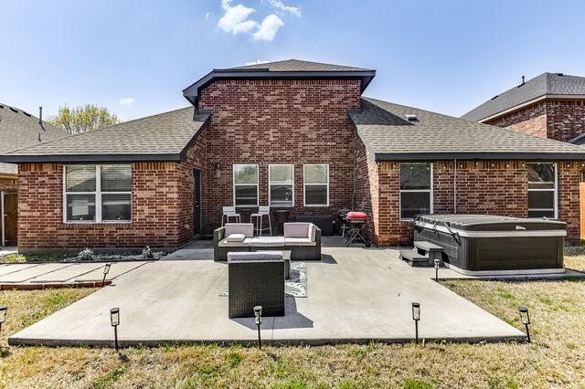 rear view of house with a hot tub, brick siding, a shingled roof, and a patio area