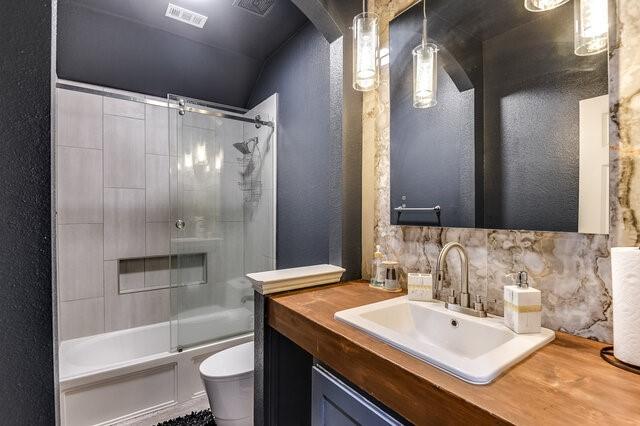 full bath featuring vanity, tasteful backsplash, toilet, a textured wall, and  shower combination