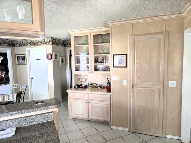 kitchen featuring glass insert cabinets, light brown cabinets, light tile patterned floors, and a textured ceiling
