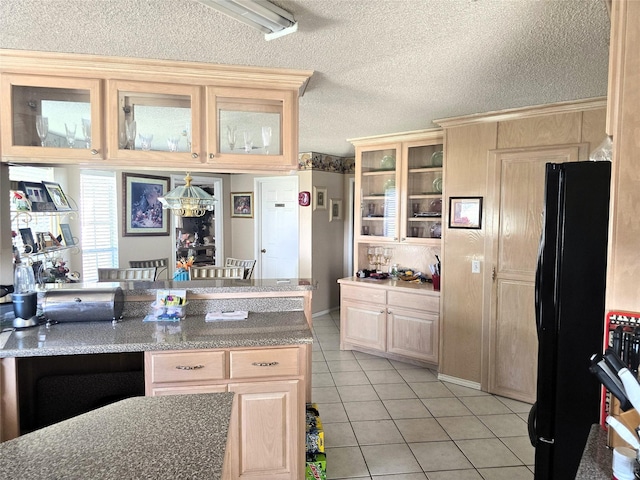 kitchen featuring light tile patterned flooring, freestanding refrigerator, light brown cabinetry, a textured ceiling, and glass insert cabinets