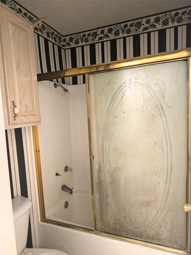 full bathroom featuring a textured ceiling, wallpapered walls, toilet, and shower / bath combination with glass door