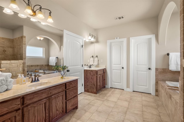 bathroom featuring visible vents, two vanities, a sink, and a garden tub