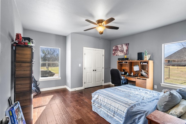 bedroom with dark wood-type flooring, a ceiling fan, baseboards, and multiple windows