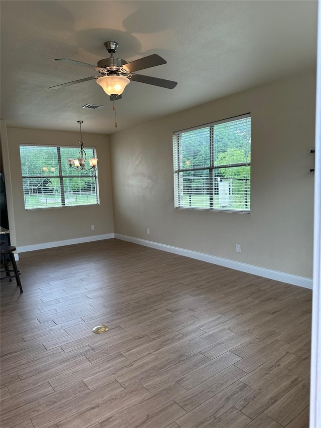 spare room featuring visible vents, ceiling fan with notable chandelier, wood finished floors, and a healthy amount of sunlight