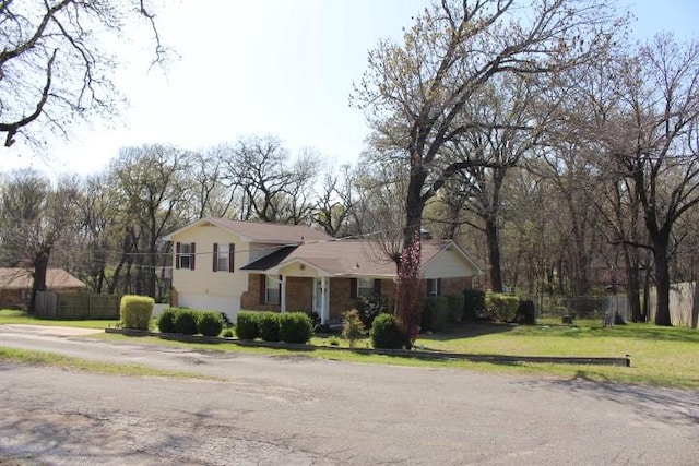 tri-level home with an attached garage, fence, and a front lawn
