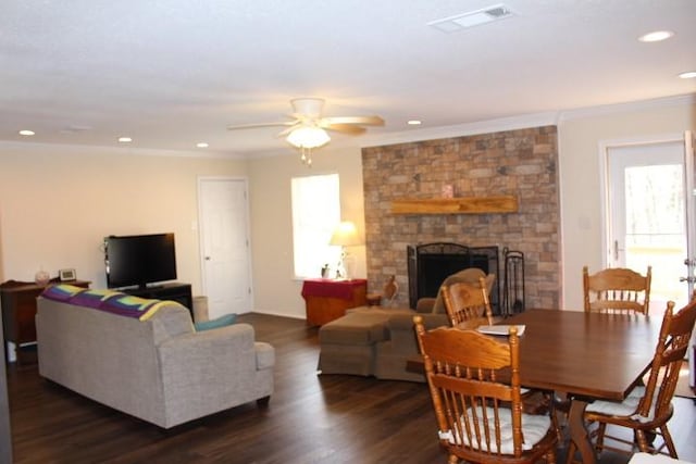 living area with a stone fireplace, visible vents, ceiling fan, ornamental molding, and dark wood-style flooring