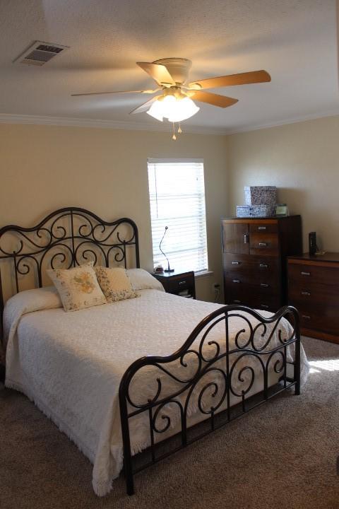 carpeted bedroom featuring ceiling fan, visible vents, and crown molding