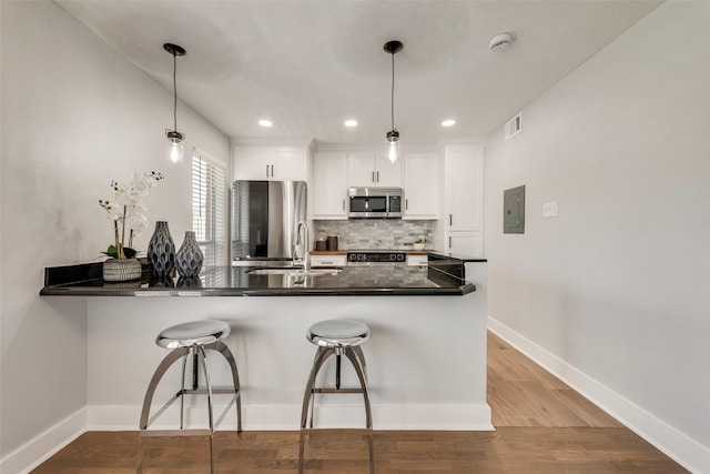 kitchen featuring appliances with stainless steel finishes, a peninsula, a kitchen breakfast bar, backsplash, and dark countertops
