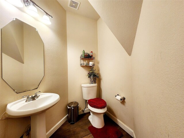 half bathroom with a sink, toilet, visible vents, baseboards, and wood finished floors
