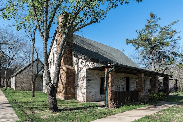 view of side of property with a lawn, brick siding, a shingled roof, and covered porch