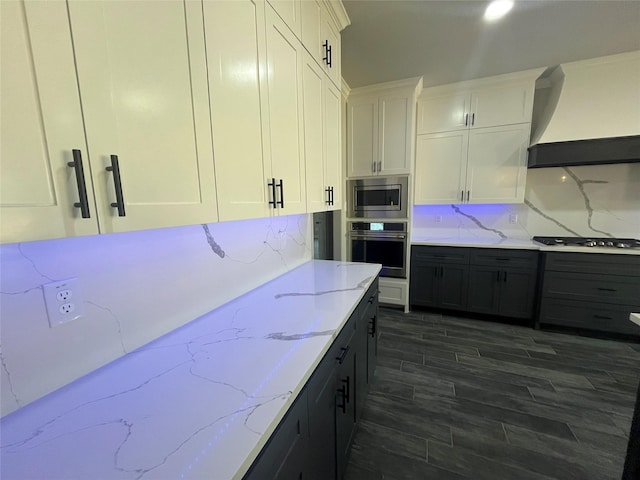 kitchen featuring light stone countertops, white cabinetry, appliances with stainless steel finishes, dark wood-style flooring, and custom range hood