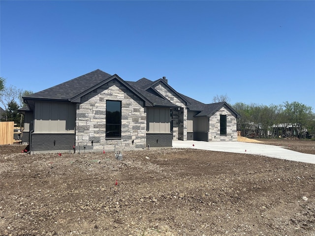 view of front of property with board and batten siding, a shingled roof, stone siding, and concrete driveway