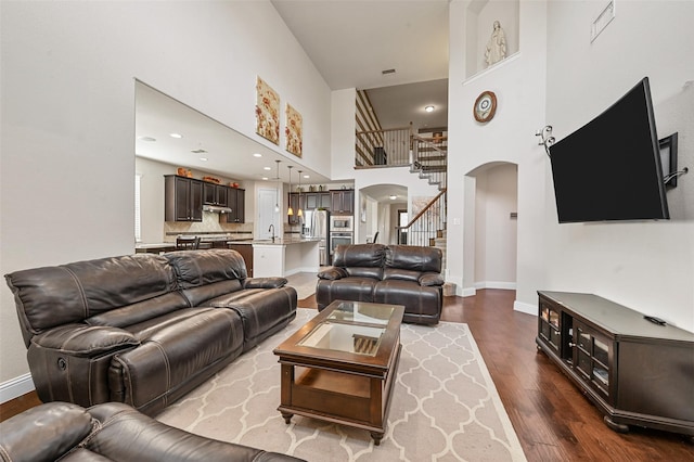 1216 Sioux St, Carrollton, TX 75010 - living room featuring arched walkways, a towering ceiling, wood finished floors, stairway, and baseboards