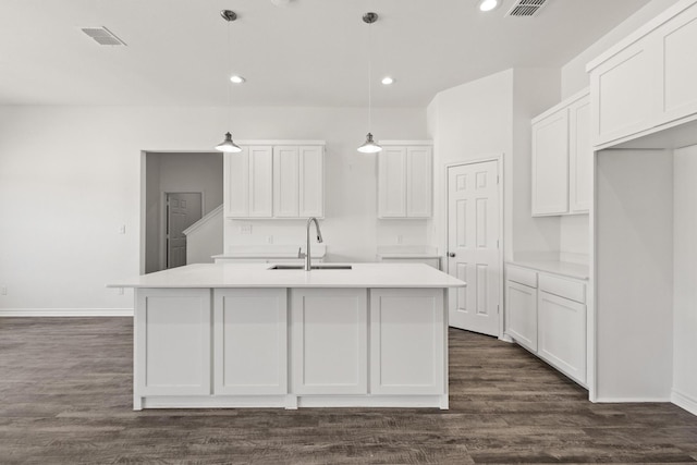 kitchen featuring baseboards, white cabinets, a center island with sink, and a sink