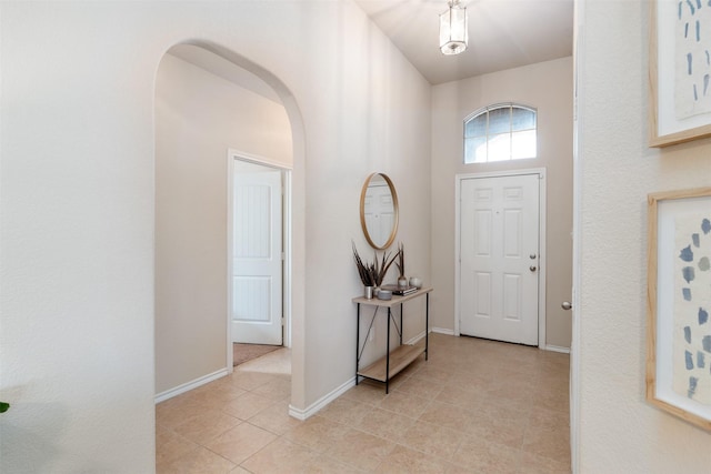 entrance foyer featuring arched walkways, a high ceiling, baseboards, and light tile patterned floors