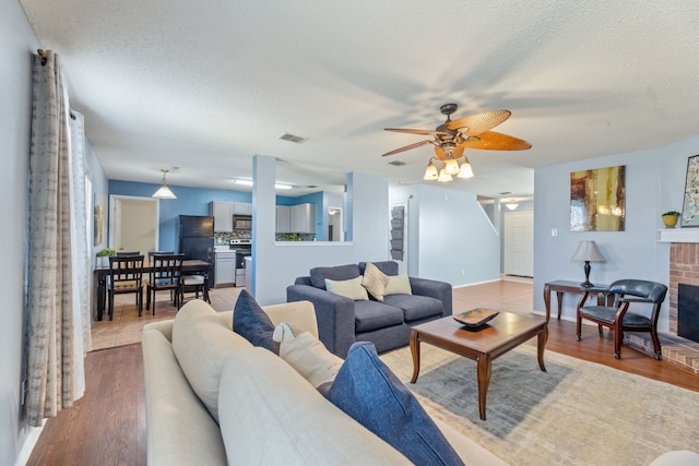 living room with ceiling fan, wood finished floors, a textured ceiling, and a fireplace