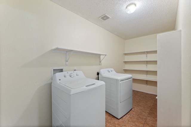 clothes washing area with washing machine and clothes dryer, a textured ceiling, and light tile patterned floors