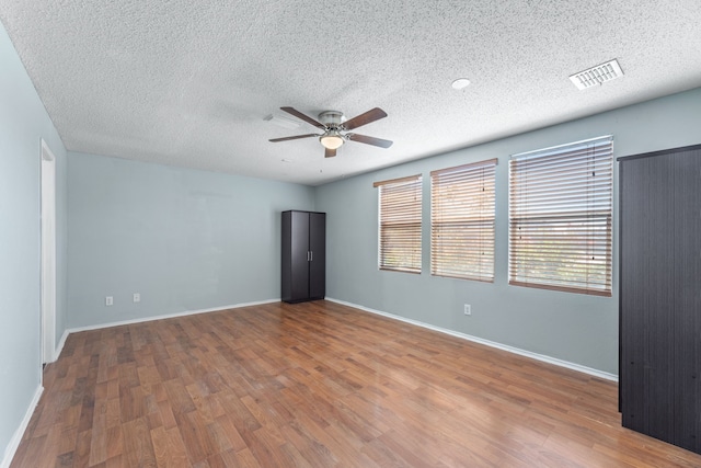 empty room featuring a ceiling fan, a textured ceiling, wood finished floors, and baseboards