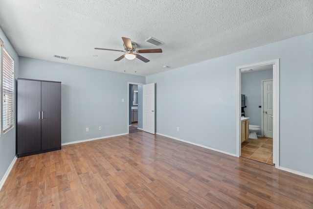unfurnished bedroom featuring wood finished floors, a textured ceiling, baseboards, and ensuite bath