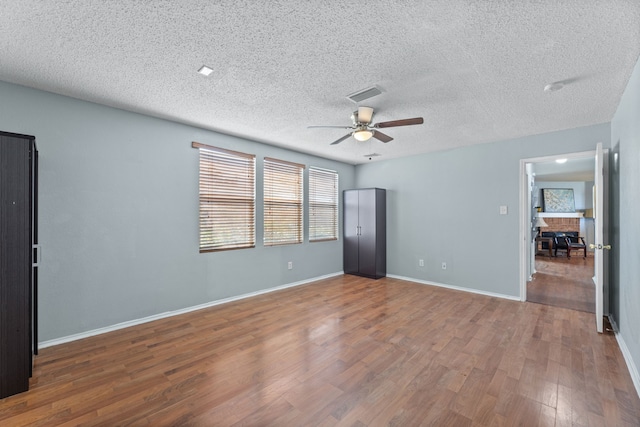 empty room with ceiling fan, wood finished floors, baseboards, and a textured ceiling