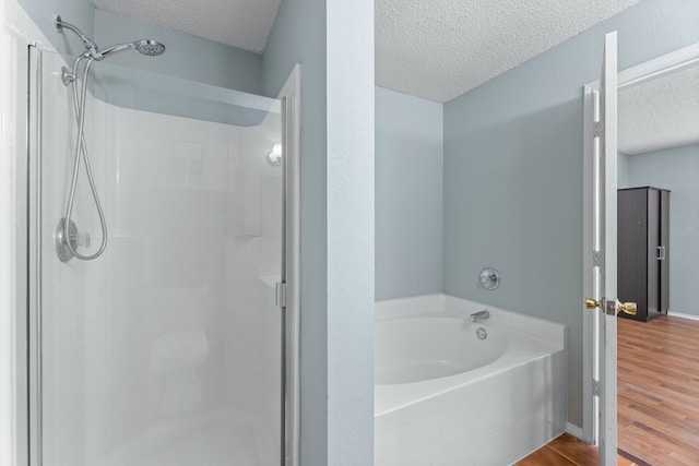 bathroom with a textured ceiling, a stall shower, wood finished floors, and a garden tub