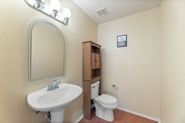 bathroom featuring a sink, toilet, a textured ceiling, tile patterned floors, and baseboards