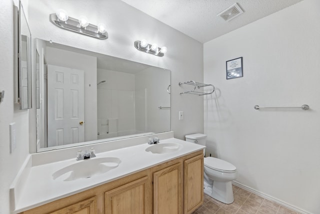 full bath with toilet, double vanity, baseboards, and a textured ceiling