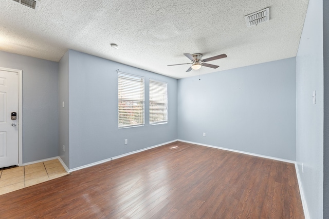 empty room with ceiling fan, wood finished floors, a textured ceiling, and baseboards