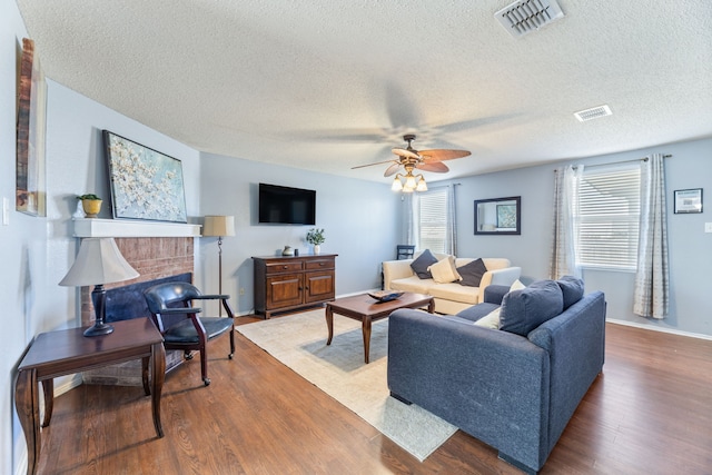 living room with a textured ceiling, wood finished floors, a brick fireplace, ceiling fan, and baseboards