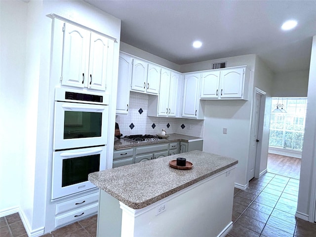 2212 Remmington Dr, Flower Mound, TX 75028 - kitchen featuring white double oven, white cabinets, a center island, stainless steel gas cooktop, and decorative backsplash