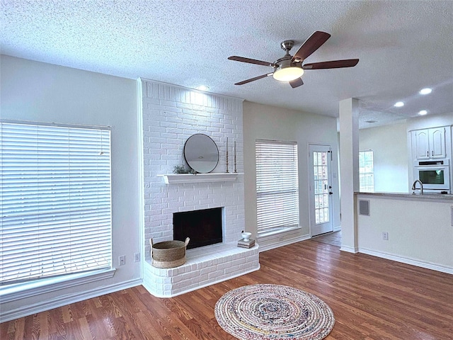 2212 Remmington Dr, Flower Mound, TX 75028 - unfurnished living room with wood finished floors, a textured ceiling, a ceiling fan, a brick fireplace, and baseboards