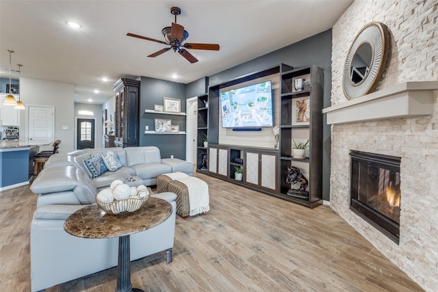 living room featuring a ceiling fan, recessed lighting, a stone fireplace, and wood finished floors