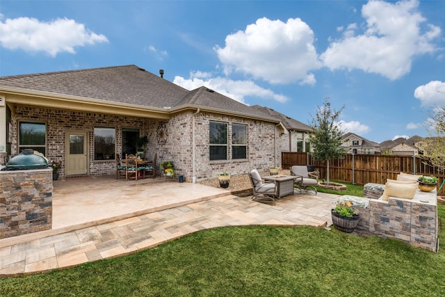 rear view of house with fence, a shingled roof, area for grilling, a patio area, and a lawn