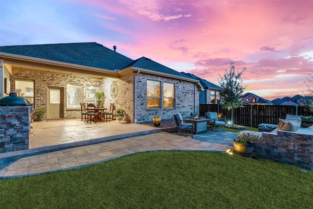rear view of house with fence, a shingled roof, brick siding, a patio, and a yard