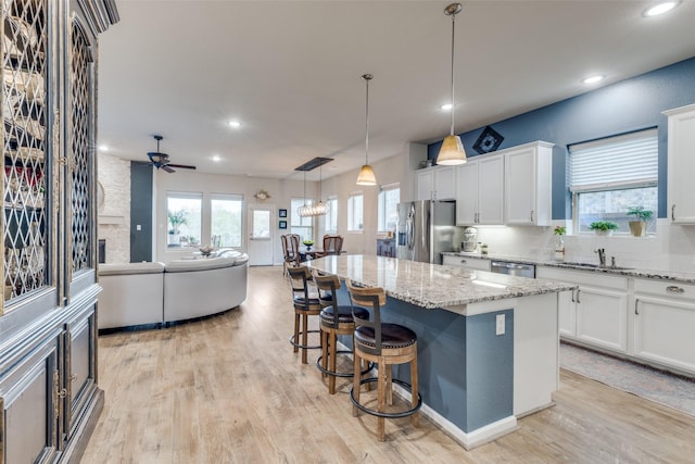 kitchen featuring pendant lighting, light stone countertops, light wood-style floors, a stone fireplace, and a center island