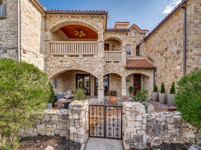 mediterranean / spanish-style home with a tile roof, a balcony, a gate, stone siding, and french doors