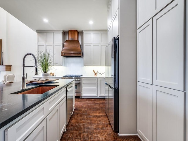 kitchen with a sink, stainless steel appliances, custom range hood, dark carpet, and white cabinetry