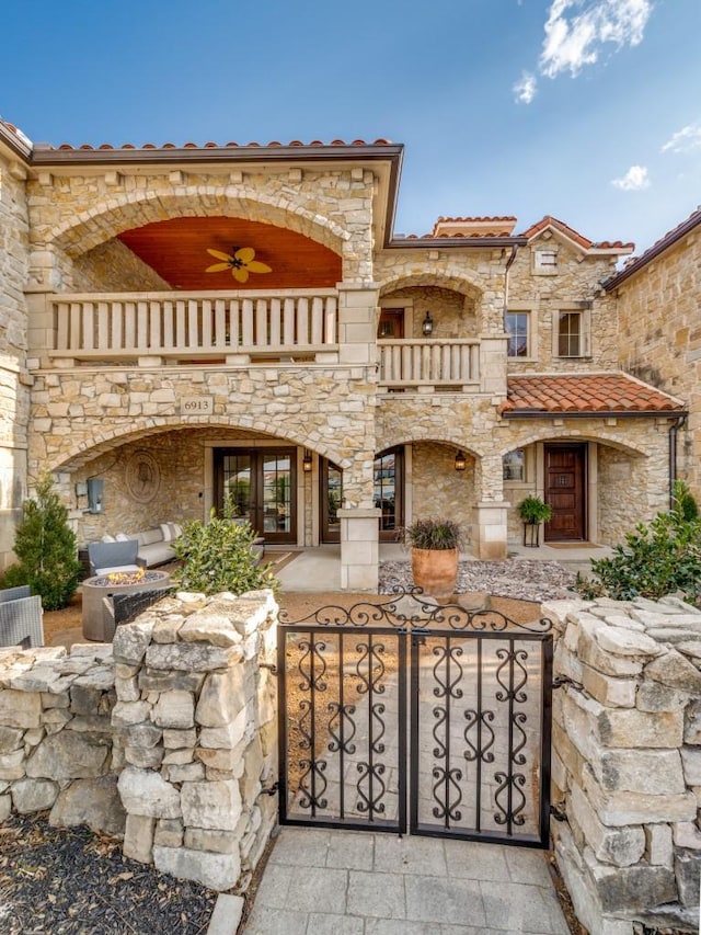 exterior space with a gate, a balcony, a fenced front yard, and stone siding