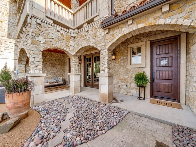 view of exterior entry with french doors, a balcony, and stone siding
