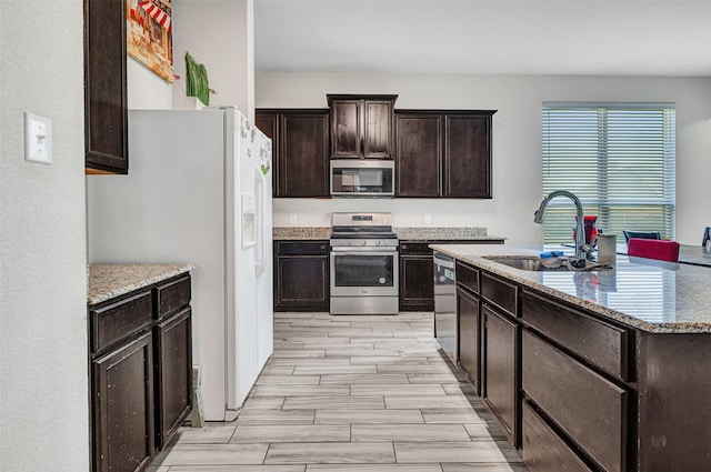 kitchen featuring light stone countertops, a sink, stainless steel appliances, wood tiled floor, and dark brown cabinets