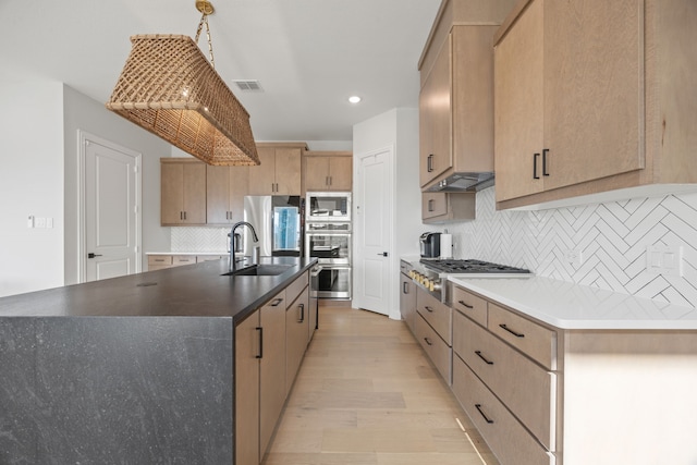 kitchen featuring stainless steel appliances, light brown cabinetry, decorative backsplash, a sink, and light wood-style flooring