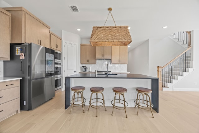 kitchen featuring a kitchen bar, a sink, visible vents, light brown cabinets, and appliances with stainless steel finishes