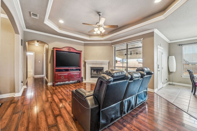 living room with arched walkways, a ceiling fan, visible vents, a raised ceiling, and dark wood-style floors