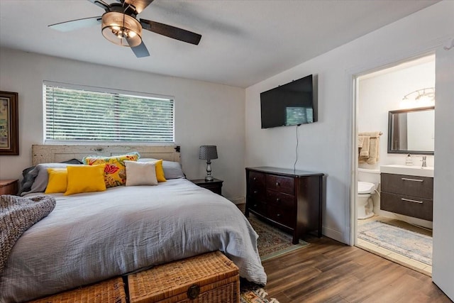 bedroom featuring a sink, ensuite bathroom, baseboards, a ceiling fan, and wood finished floors